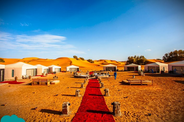 Elegant luxury desert camps in Morocco illuminated at night, surrounded by soft sand dunes and starry skies.